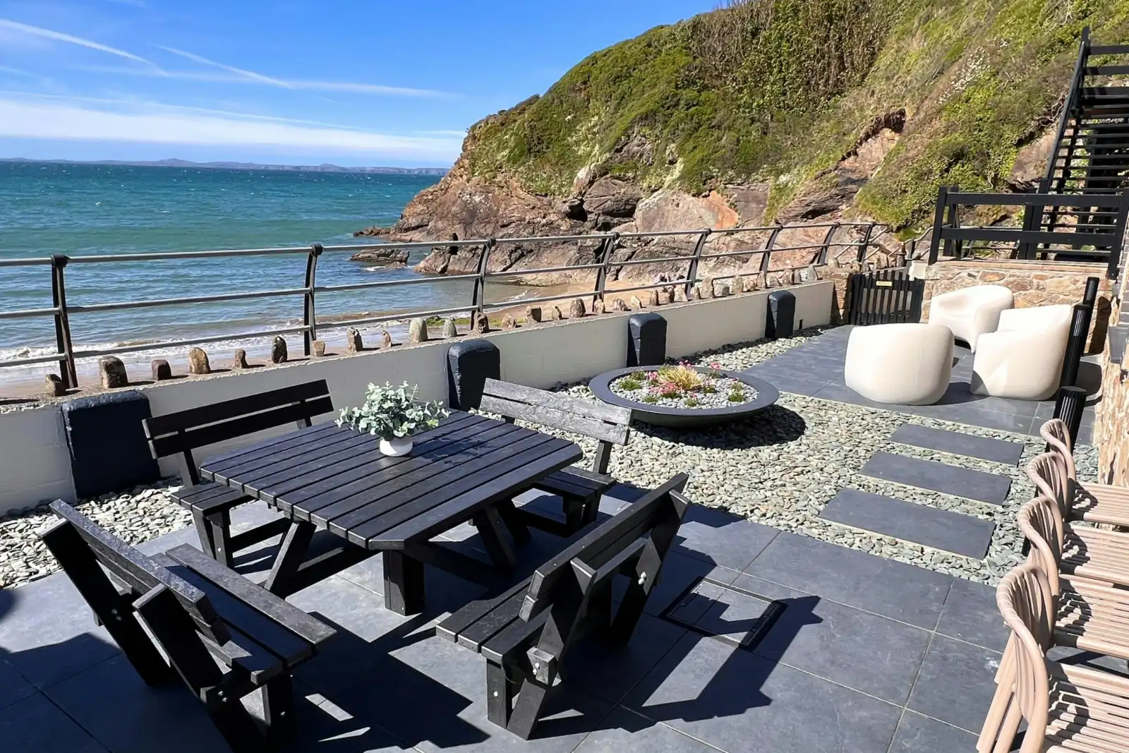 Seaside terrace with picnic table, benches and lounge seating overlooking the sea and rocky cliffs
