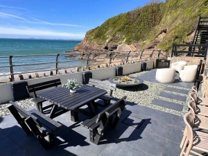Seaside terrace with picnic table, benches and lounge seating overlooking the sea and rocky cliffs