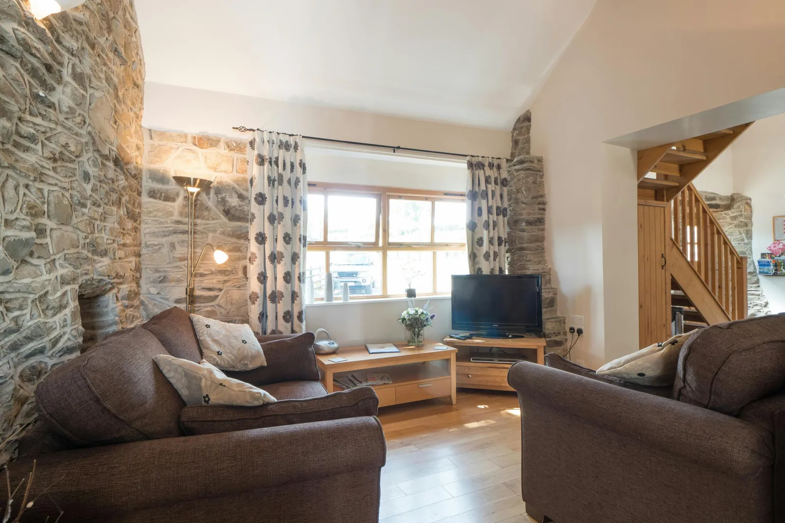 Sofas facing window, coffee table and unit with TV, standard lamp, wooden staircase to upstaris