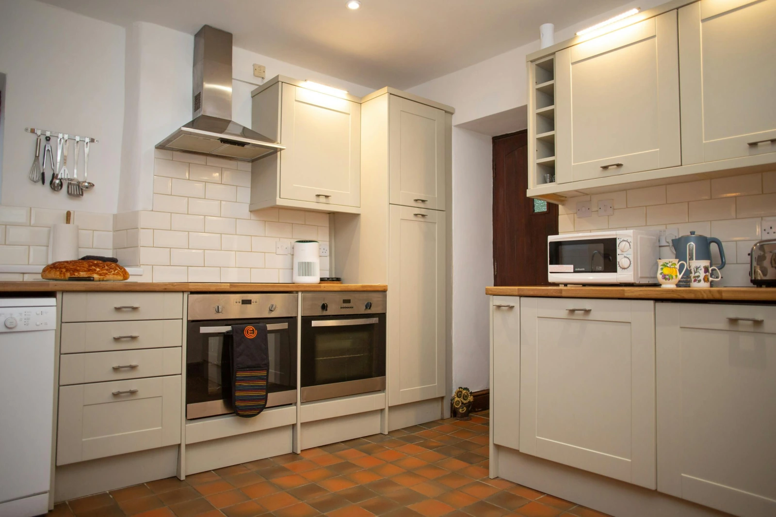 Cream kitchen with white tiled splashback, double oven and extractor hood