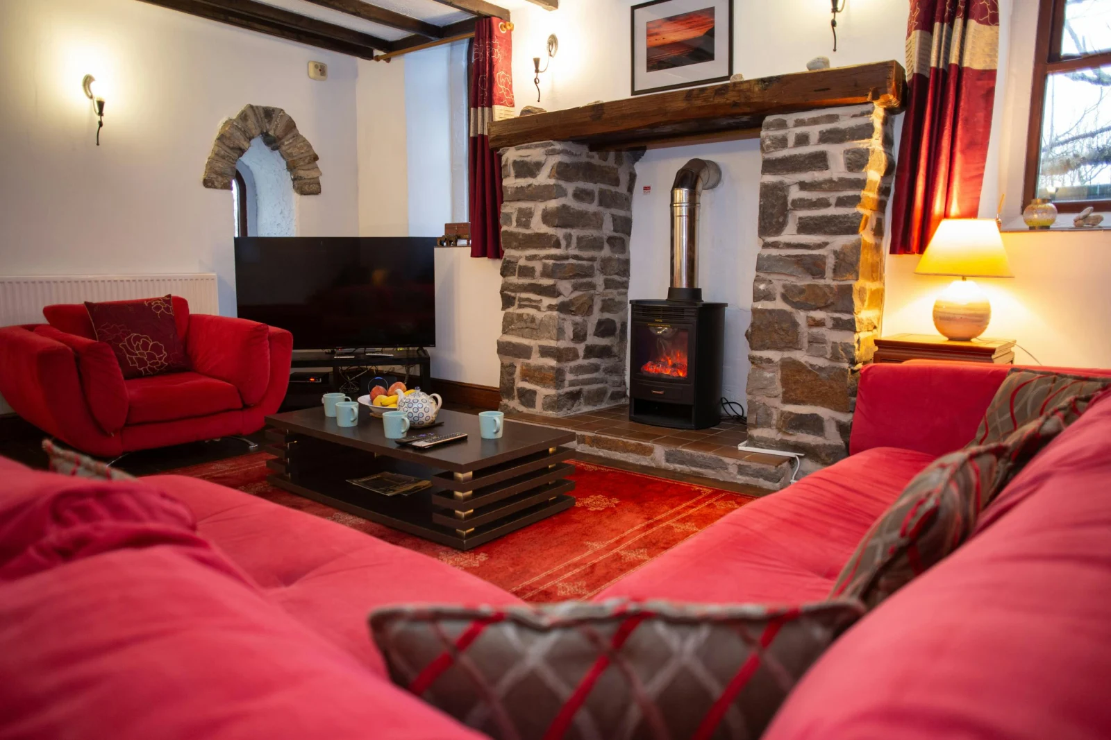 Living room with red sofas, stone fireplace, wood-burning stove, and a television in the corner