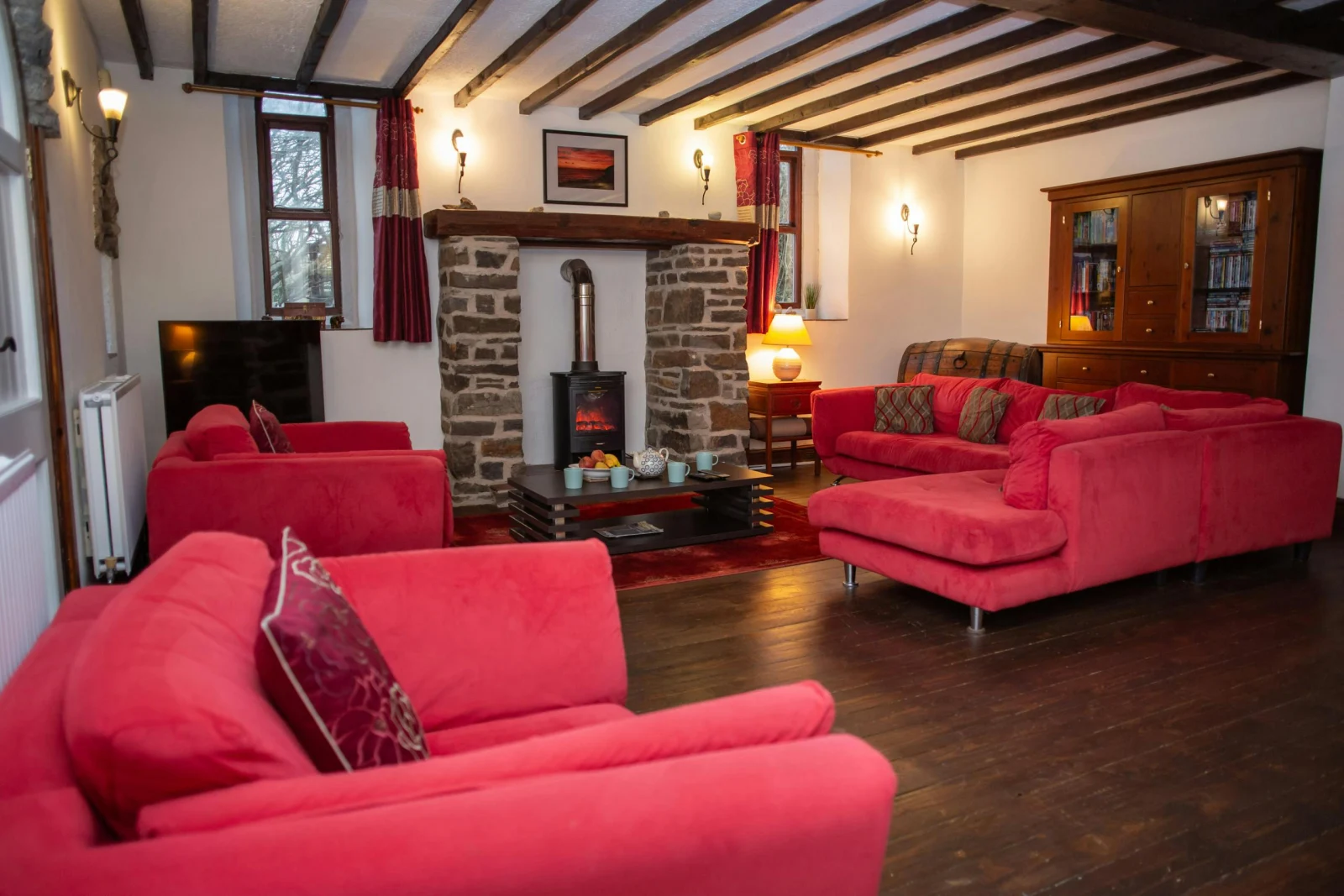Red sofas around a stone fireplace in a beamed ceiling lounge