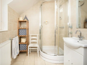One of 3 bathrooms with shower cubicle, chair and hand basin with mirror above