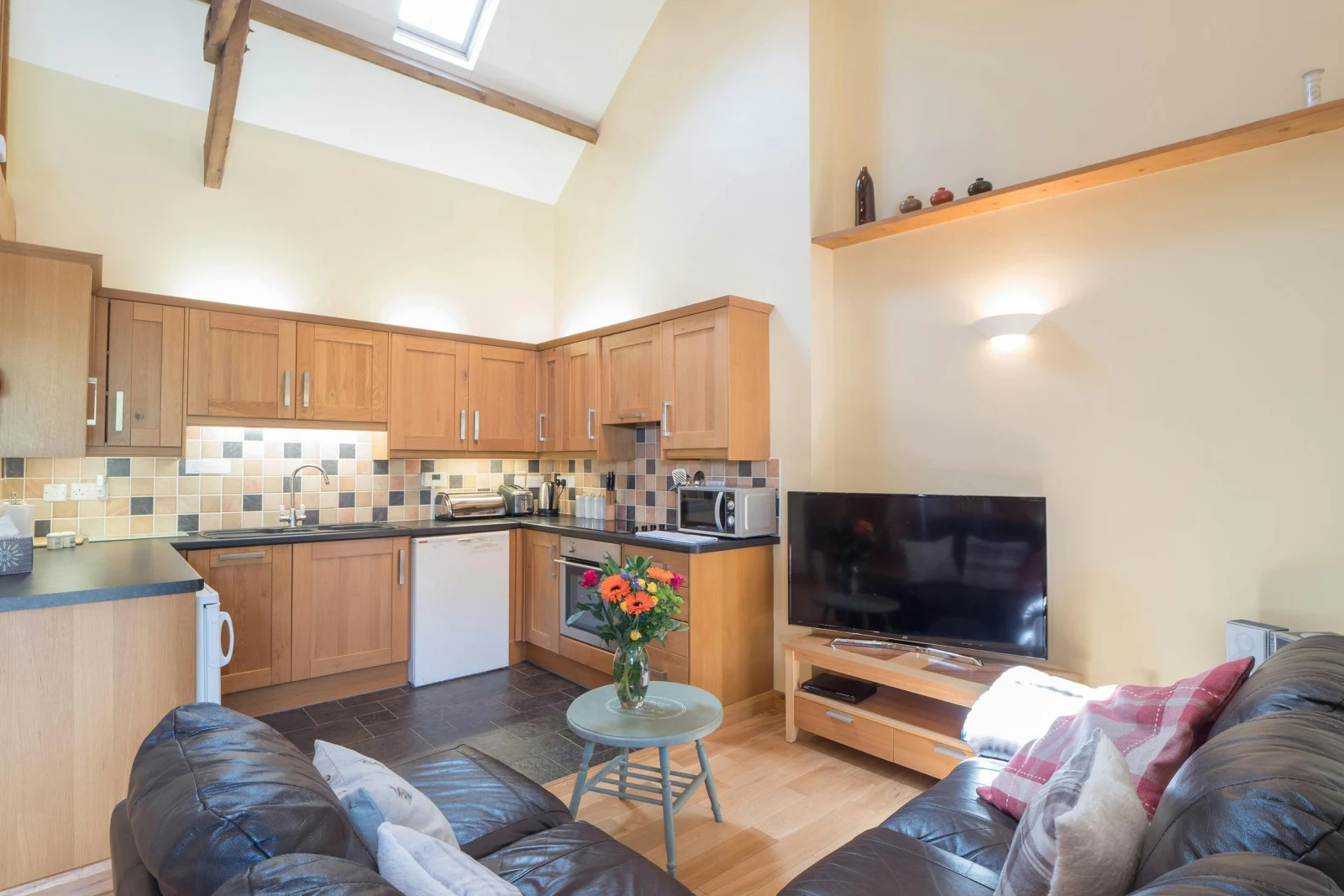 Open plan kitchen and sitting area in Eirlys, fitted units, leather corner sofa, TV and coffee table