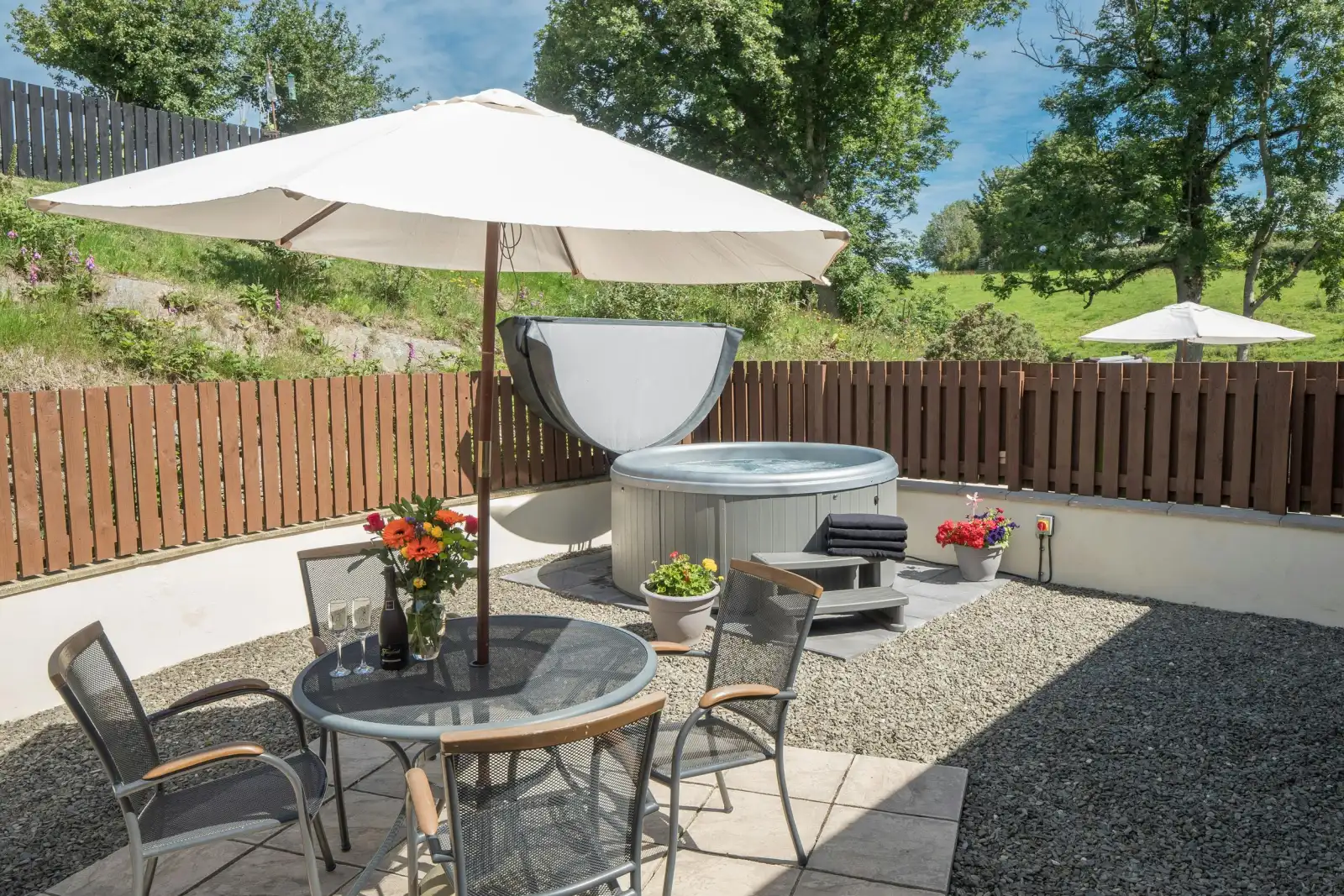 Patio with rural views at Eirlys, hot tub, table, chairs and parasol